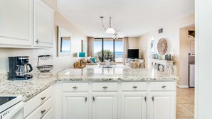 A kitchen with white cabinets, a granite countertop, and a view to the outside. - Beautiful home in beachfront luxury complex with pool, sauna & WiFi (Orange Beach)