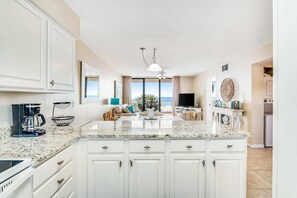 A kitchen with white cabinets, a granite countertop, and a view to the outside. - Beautiful home in beachfront luxury complex with pool, sauna & WiFi (Orange Beach)
