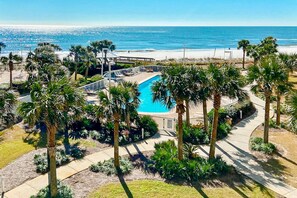 Une piscine entourée de palmiers, une vue sur la plage et un ciel dégagé.