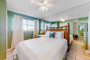 A hotel room with a large bed, a wooden headboard, a nightstand, a mirror, and a view of the hallway. - Splendid beachfront condo with pool, tennis court, sauna, & WiFi (Orange Beach)