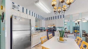 Eine moderne Küche mit einem Edelstahl-Kühlschrank, weißen Schränken und einem Essbereich mit weißem Tisch und Holzsesseln.