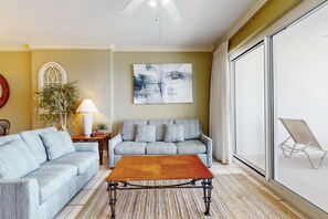 A living room with a sofa, a coffee table, a lamp, a plant, and a large abstract painting. - 9th-floor, Gulf-front condo with balcony, pools, hot tubs, gym & beach access (Orange Beach)