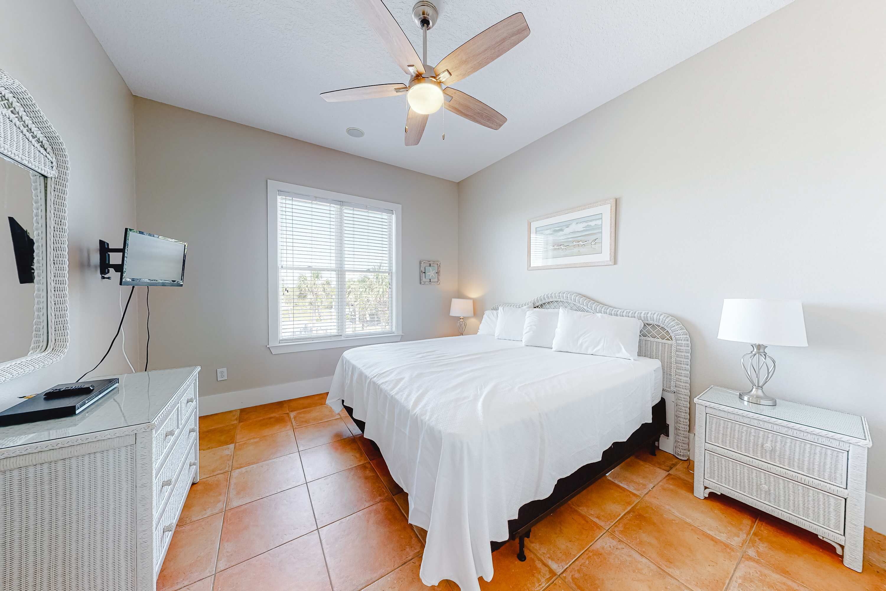A bedroom with a bed, nightstand, lamp, ceiling fan, TV, and a window.