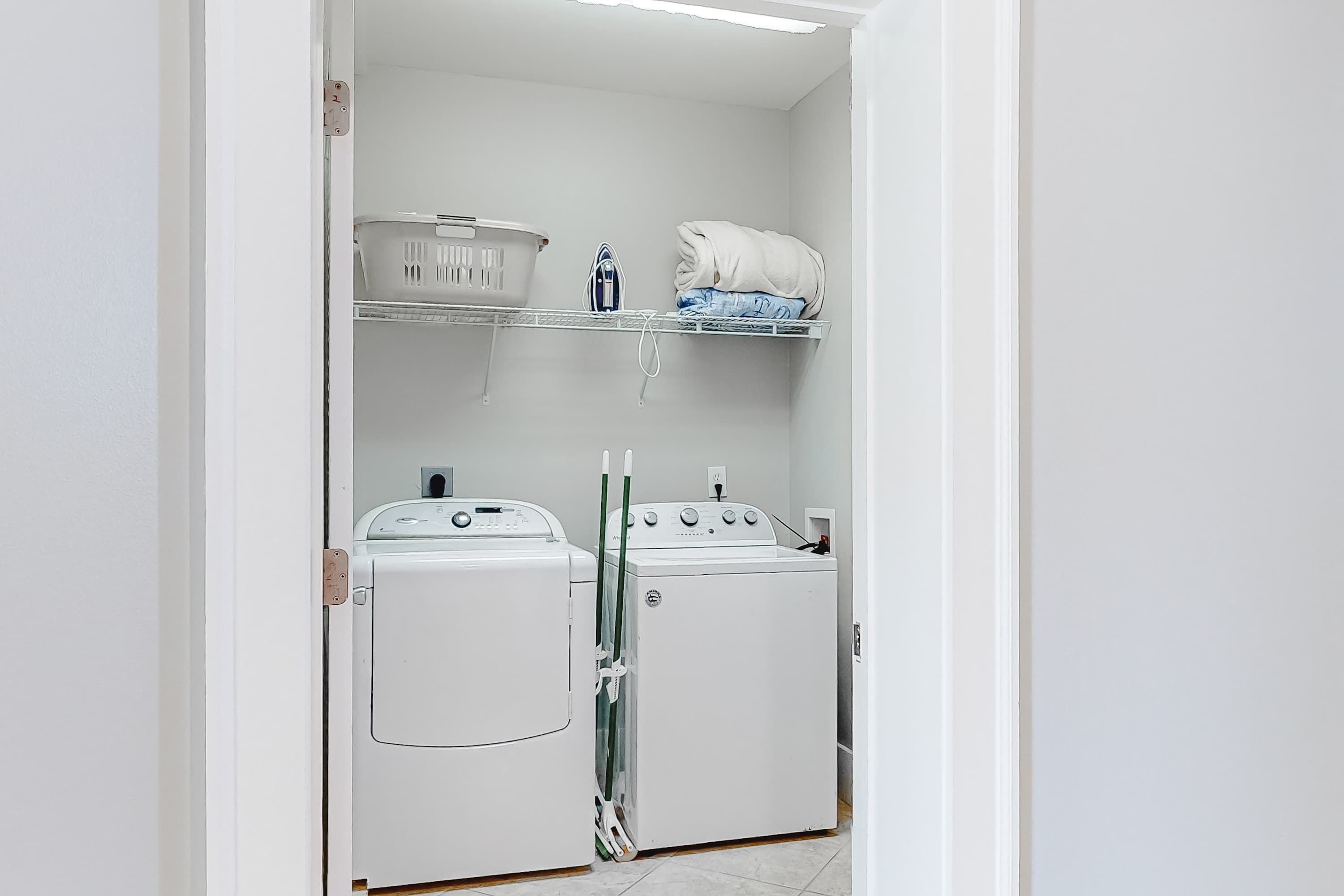 Une buanderie équipée de deux machines à laver blanches, d’un étendoir et d’une étagère avec un panier et des serviettes.
