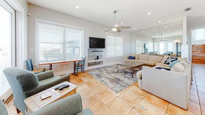 A modern living room with a sofa, chairs, a coffee table, a TV, and a ceiling fan. - Spacious beachfront home with Gulf-view decks, boardwalk, & pool (Orange Beach)