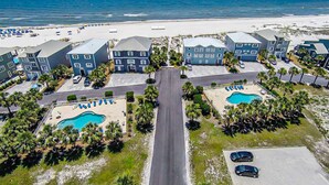 A coastal hotel with multiple buildings, a central road, and a swimming pool. - Spacious beachfront home with Gulf-view decks, boardwalk, & pool (Orange Beach)