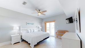A bedroom with a bed, nightstands, a ceiling fan, a television, and a window. - Spacious beachfront home with Gulf-view decks, boardwalk, & pool (Orange Beach)