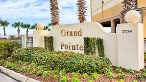 L’entrée d’un hôtel, avec une enseigne indiquant « Grand Pointe », des palmiers et un jardin bien entretenu.