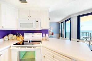 Eine Küche mit weißen Schränken, einer Mikrowelle, einem Backofen und Meerblick durch große Fenster.