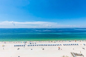 Ein Strand mit Reihen von Sonnenschirmen und Liegestühlen, einem klaren Himmel und ruhiger See.
