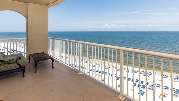 Ein Balkon mit Blick auf Strand und Meer, eine Sitzecke und ein kleiner Tisch.