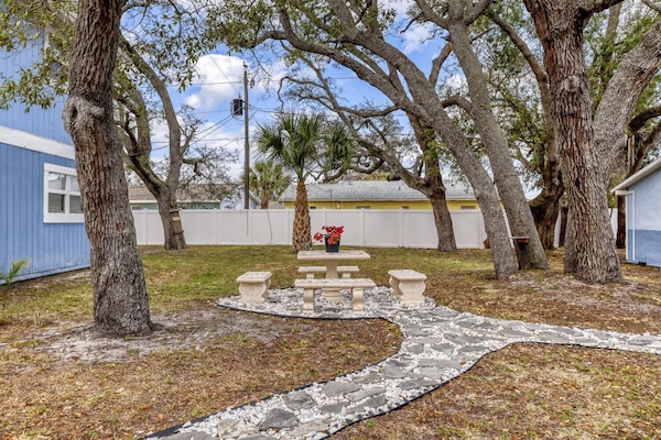 Quiet patio space with a stone picnic table surrounded by mature trees and bordered by blue and yellow buildings.