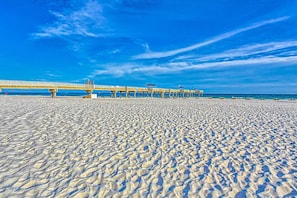 A beach with a pier extending into the water, sandy beach, and clear blue sky. - 3rd-Floor Beachfront Condo w/Spacious Balcony, Shared Outdoor Pool, Gym, A/C (Orange Beach)