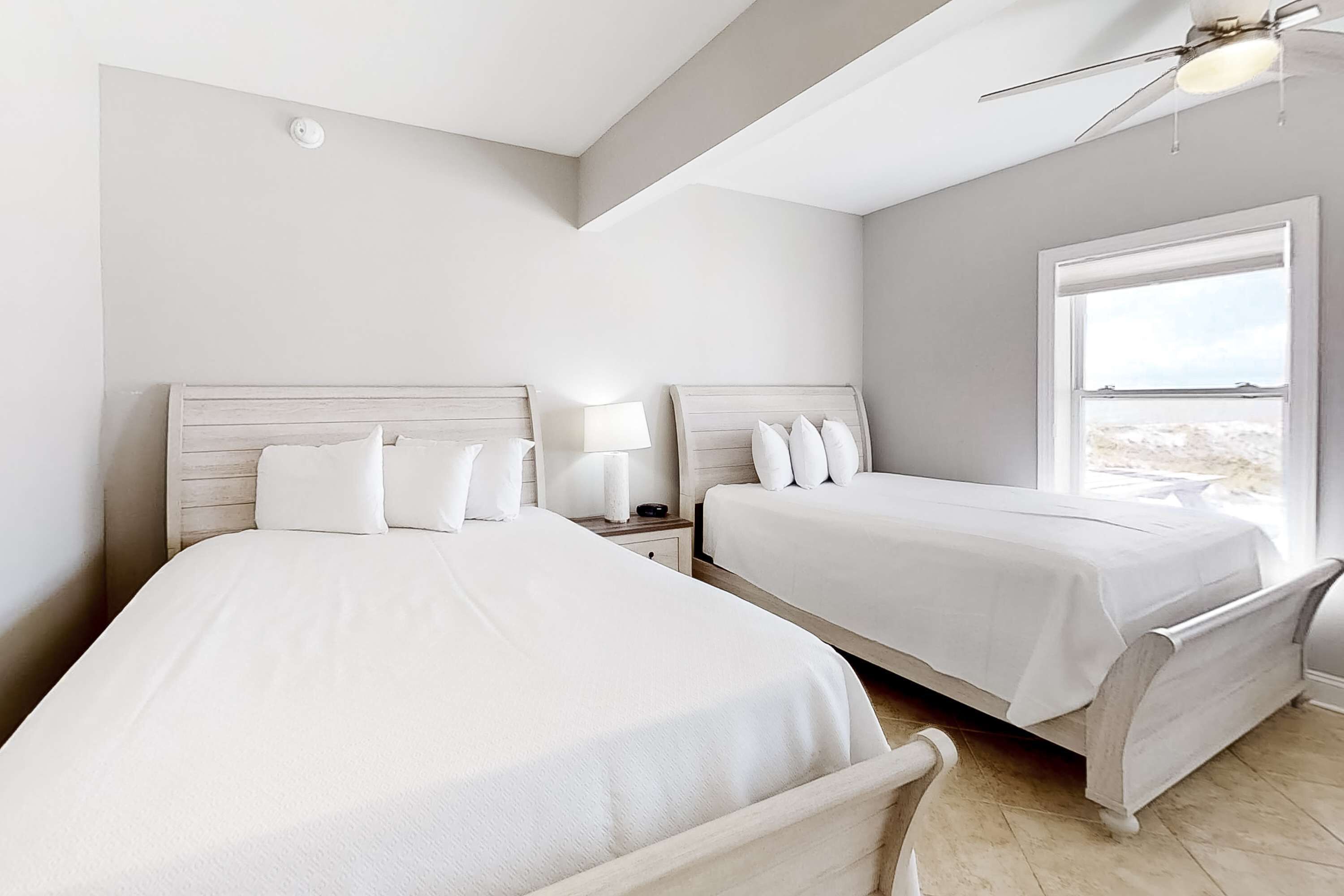 A bedroom with two beds, a ceiling fan, a nightstand, and a window.