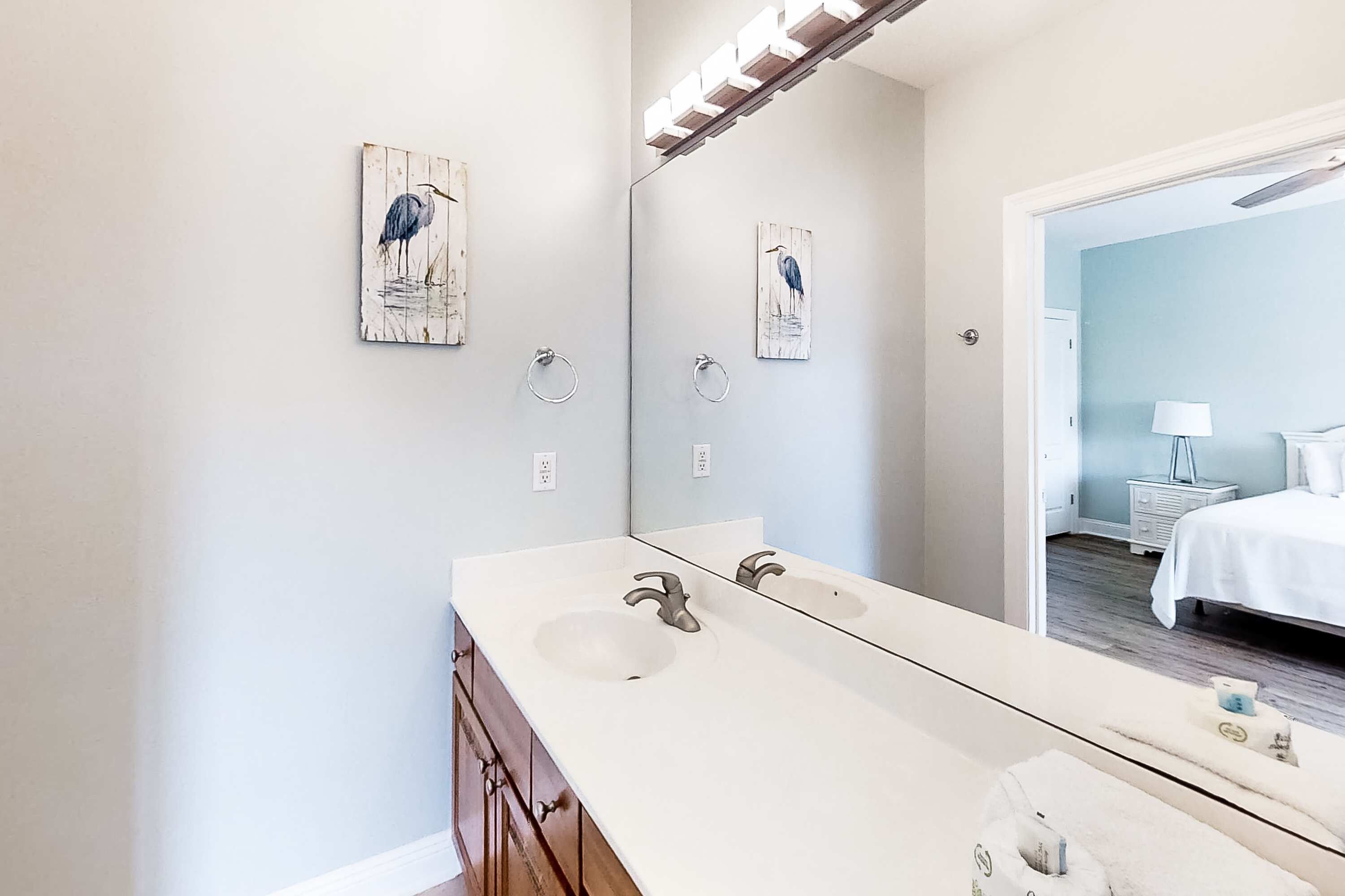 A bathroom with a double sink, wooden cabinets, and wall-mounted artwork.