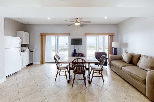 A modern living room with a dining area, a sofa, a TV, and a ceiling fan. - Spacious beachfront home with large balconies & pool access (Orange Beach)