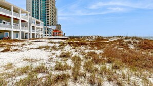 Ein Strandhotel mit mehreren Balkonen, einem Sandstrand und einem hohen Gebäude im Hintergrund.