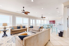 A spacious living area with a sofa, a coffee table, and a dining area with chairs and a table. - Spacious beachfront wedding-friendly home with multiple decks & shared pool (Orange Beach)