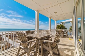 A covered outdoor area with a table and chairs, overlooking the beach. - Spacious beachfront wedding-friendly home with multiple decks & shared pool (Orange Beach)