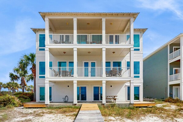 A multi-story beachfront building with balconies, a wooden deck, and a sandy beach in the background. - Spacious beachfront wedding-friendly home with multiple decks & shared pool (Orange Beach)