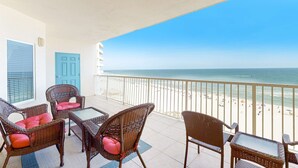 Un balcón con mobiliario de mimbre, vista a la playa y una puerta azul.