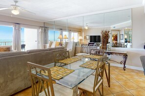 Ein Wohnzimmer mit einem Glastisch, bequemen Sitzgelegenheiten, einem Deckenventilator und Blick auf den Ozean.