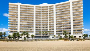 Un hotel de varios pisos con balcones, situado en una playa con palmeras.