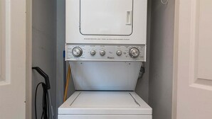En frontbetjent vaskemaskine og tørretumbler fra Whirlpool i et vaskerum, med en dør til venstre og en moppe hængende på væggen til højre.