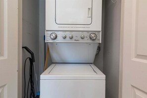 Eine Frontlader-Waschmaschine und ein Trockner von Whirlpool in einem Waschraum, mit einer Tür links und einem an der Wand befestigten Mop rechts.