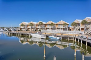 Ein Yachthafen mit einer Reihe von Gebäuden direkt am Strand, Booten, die vertäut sind, und ruhigem Wasser.