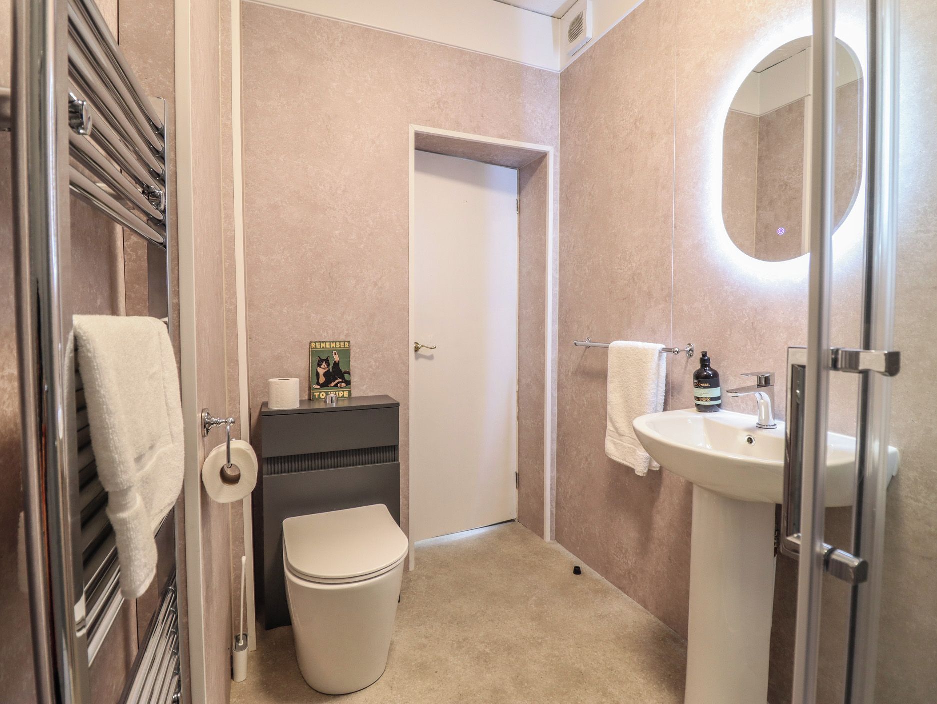 Un baño con inodoro, lavamanos, toallero y una puerta que da a otra habitación.