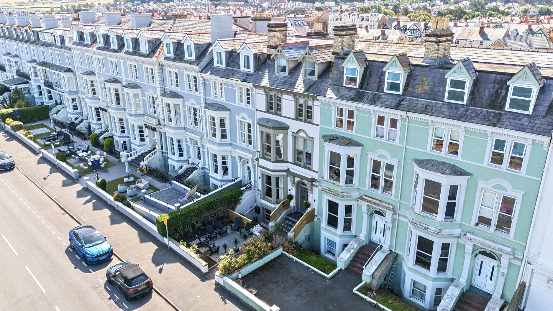 A row of terraced houses with bay windows, a driveway, and parked cars.