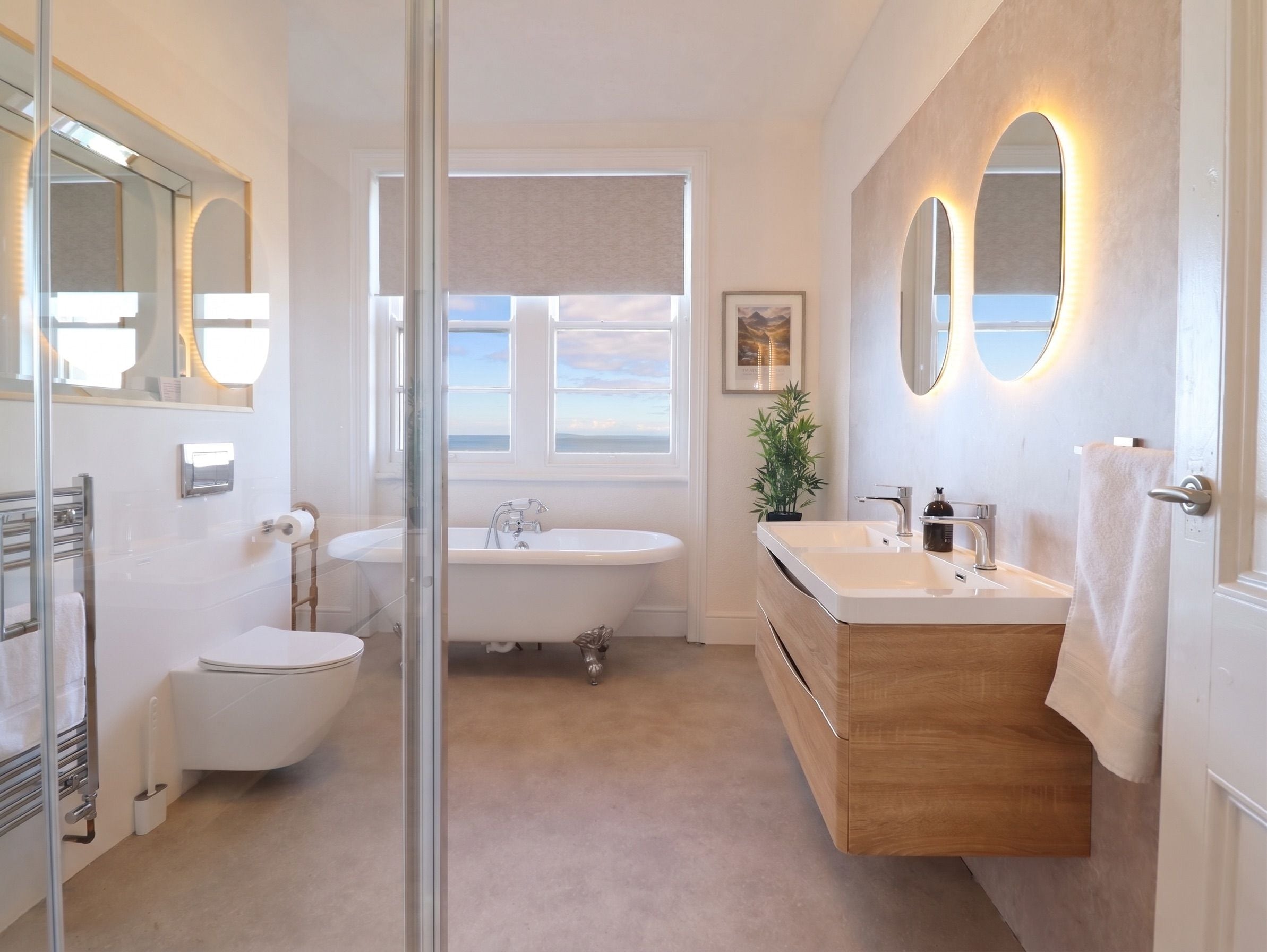 Un baño con bañera, lavamanos e inodoro. Hay una ventana con vista al mar.