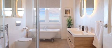 Un baño con bañera, lavamanos e inodoro. Hay una ventana con vista al mar.