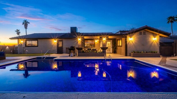 Una casa moderna con piscina, zona de estar exterior y un patio bien iluminado.