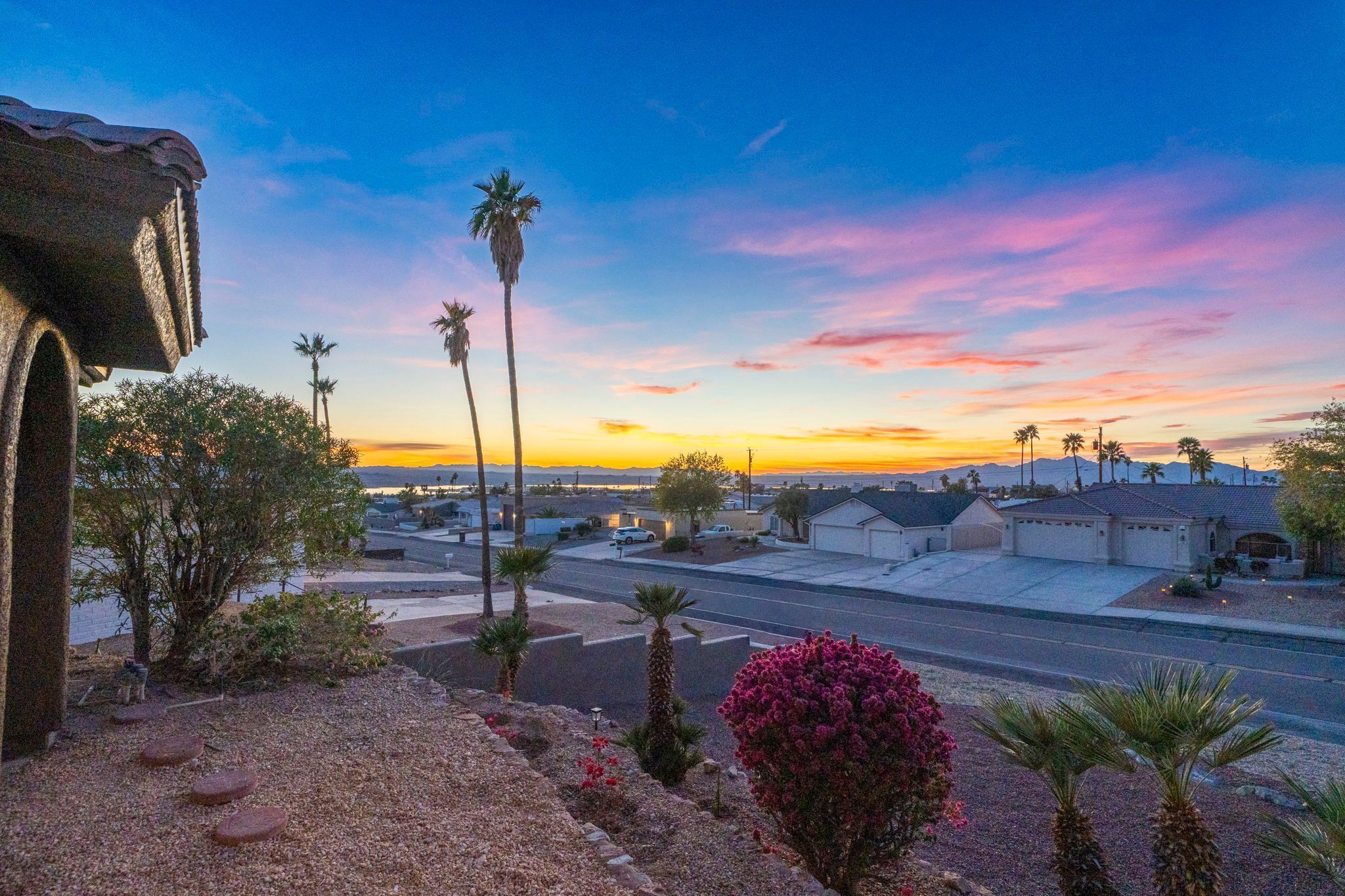 A residential area with palm trees, a road, and houses under a sunset sky.