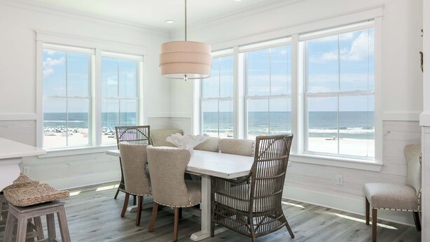 A dining area with a table and chairs, large windows with a view of the beach, and a hanging light fixture. - Luxury Gulf-front home w private splash pool & direct beach access (Orange Beach)