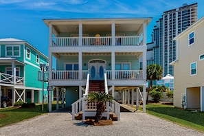 A multi-story building with a central staircase, balconies, and a small palm tree in the foreground. - Family-friendly beach home w Gulf views, a full kitchen, & spacious living area (Orange Beach)