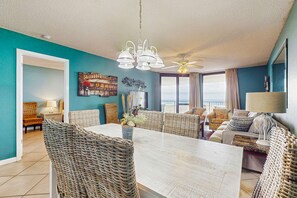 A spacious living room with a large dining table, wicker furniture, a ceiling fan, and a view to the outside. - Waterfront condo w/ balcony, multiple pools, lighted tennis courts, hot tub (Orange Beach)