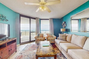A living room with a TV, sofa, chairs, a coffee table, and a ceiling fan. - Waterfront condo w/ balcony, multiple pools, lighted tennis courts, hot tub (Orange Beach)