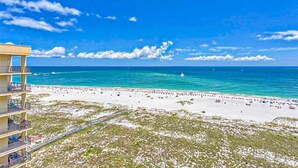 A beach with a clear blue sky, a sandy shore, and a building with balconies overlooking the beach. - Waterfront condo w/ balcony, multiple pools, lighted tennis courts, hot tub (Orange Beach)