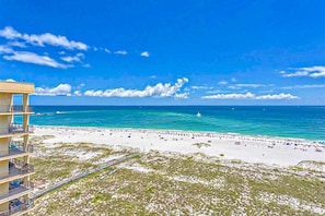 A beach with a clear blue sky, a sandy shore, and a building with balconies overlooking the beach. - Waterfront condo w/ balcony, multiple pools, lighted tennis courts, hot tub (Orange Beach)