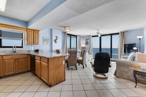 A modern kitchen with wooden cabinets, a dining area with wicker chairs, a black armchair, and a view of the ocean. - Gulf & beachfront condo with indoor & outdoor pools, sauna & sun deck (Orange Beach)