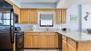 Una cocina con armarios de madera, un refrigerador de acero inoxidable, un microondas, un fregadero y una ventana con persianas.