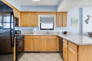 A kitchen with wooden cabinets, a stainless steel refrigerator, a microwave, a sink, and a window with blinds. - Gulf & beachfront condo with indoor & outdoor pools, sauna & sun deck (Orange Beach)