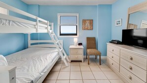 Un dormitorio con una litera, una mesita de noche con lámpara, una silla, un aparador y un televisor.