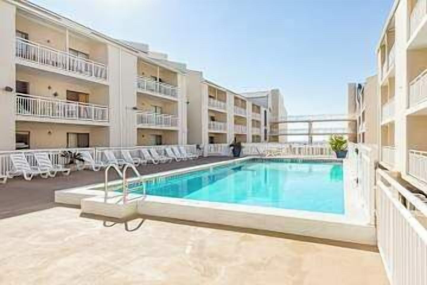 A hotel with a swimming pool, multiple balconies, and lounge chairs.
