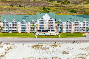 A beachfront hotel with multiple balconies, a swimming pool, and a green lawn. - Beautiful oceanfront condo with pool, hot tub, beach access, balcony, & WiFi (Gulf Shores)