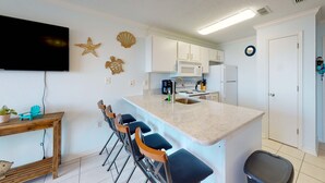 Een keuken met een bar, witte kastjes, een magnetron en een spoelbak.