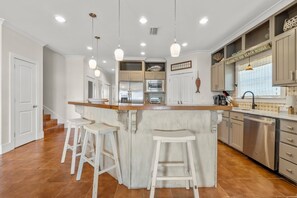 A kitchen with a central island, bar stools, a stainless steel dishwasher, and a sign reading 'Welcome to our Beach House.' - Delightful escape with direct beach access, WiFi, furnished deck, & full kitchen (Gulf Shores)